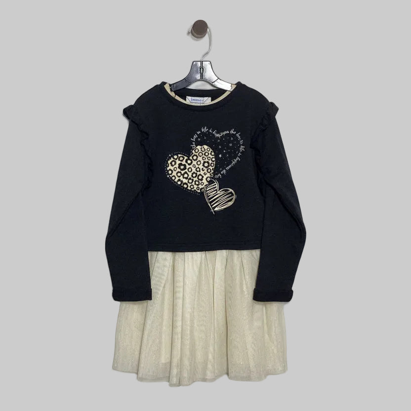Black sweater with heart design over a beige pleated skirt on a hanger against a white background